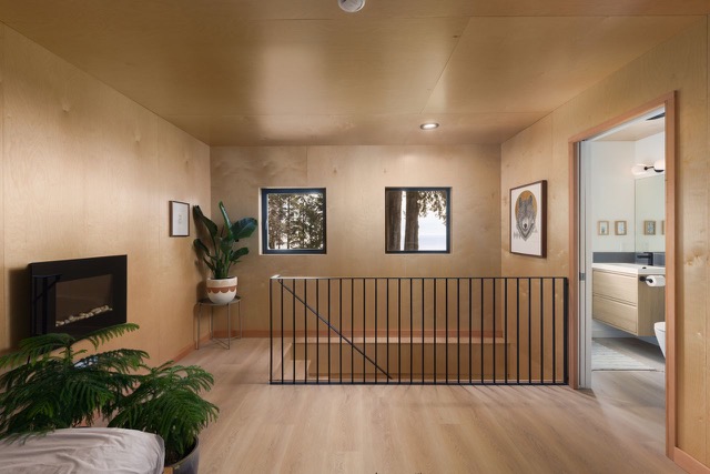 Plywood-lined garden cottage loft with black railing and tree views
