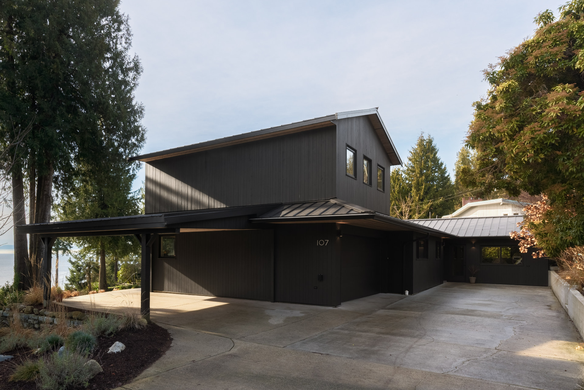 Dark cedar home with metal roof and carport among tall evergreens